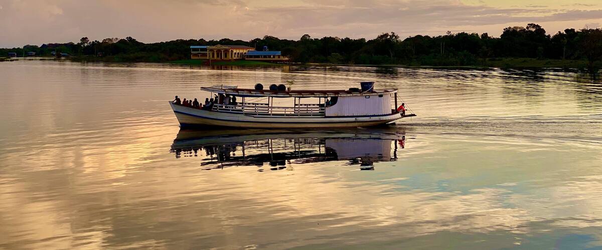 A boat on calm water with a reflection, a building in the background, and a cloudy sky.
