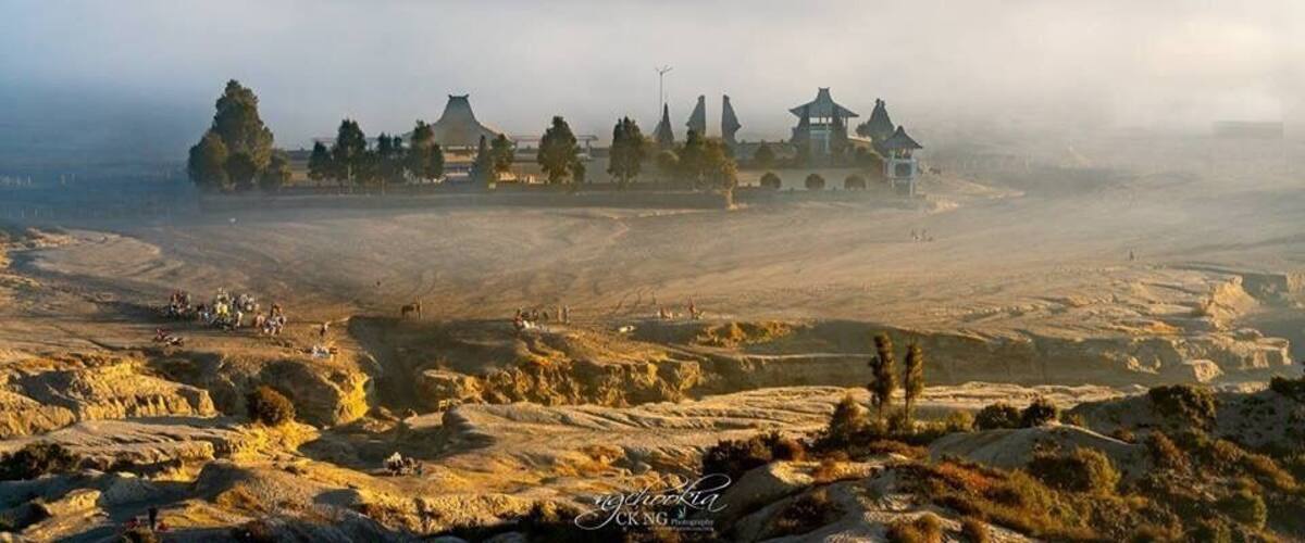 A historic site with traditional architecture, including pagodas and a large central building, surrounded by a hilly landscape and a blanket of clouds.