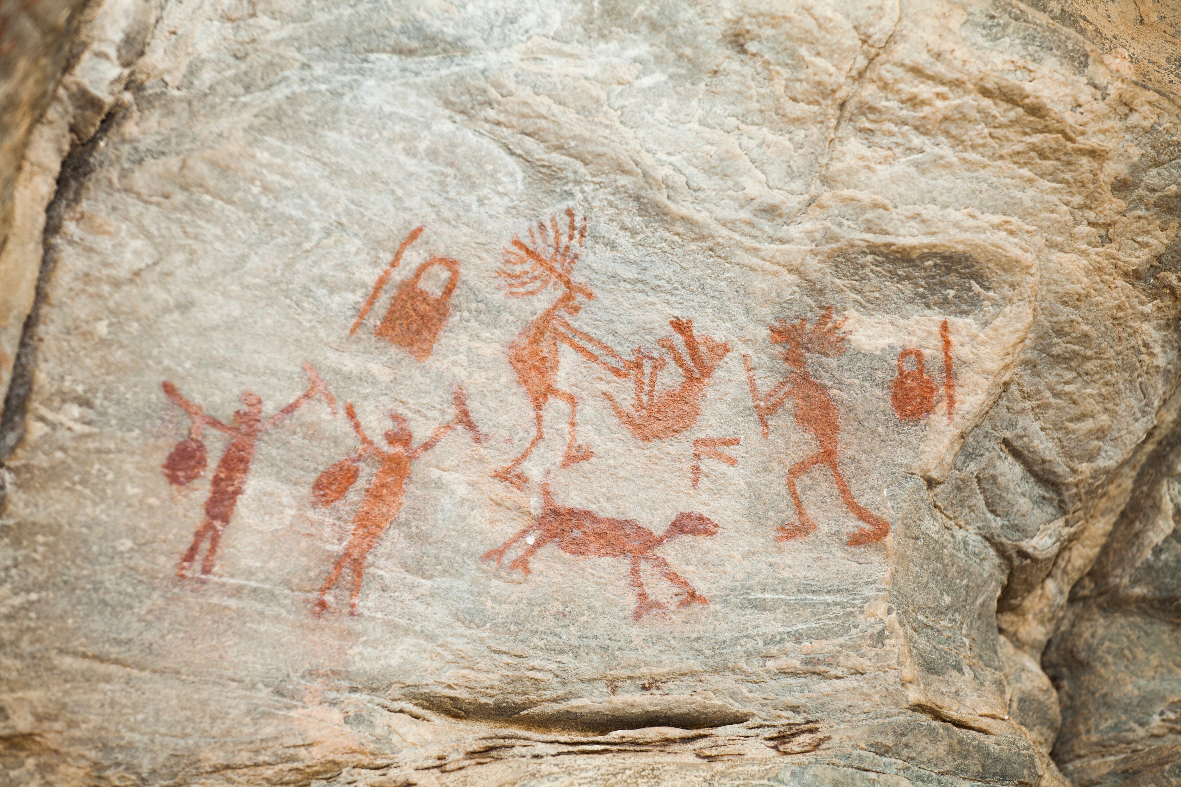 A rock with ancient red ochre cave paintings of human figures and animals.