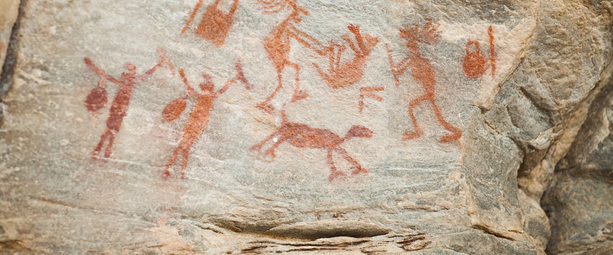 A rock with ancient red ochre cave paintings of human figures and animals.