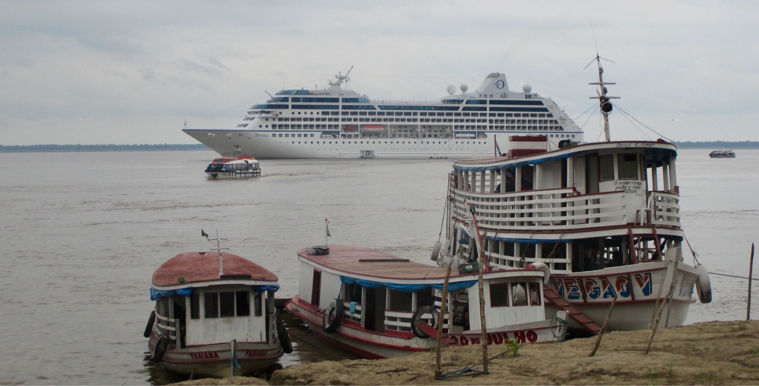 A large cruise ship named 'Sirius' docked at a port with smaller boats nearby.