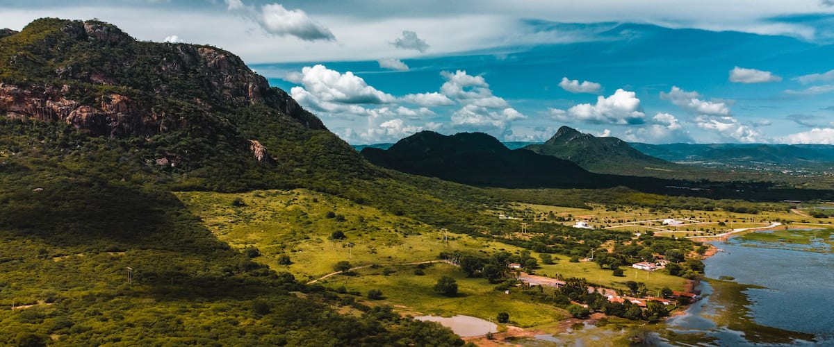 A lush green landscape with a river, mountains, and a small settlement.