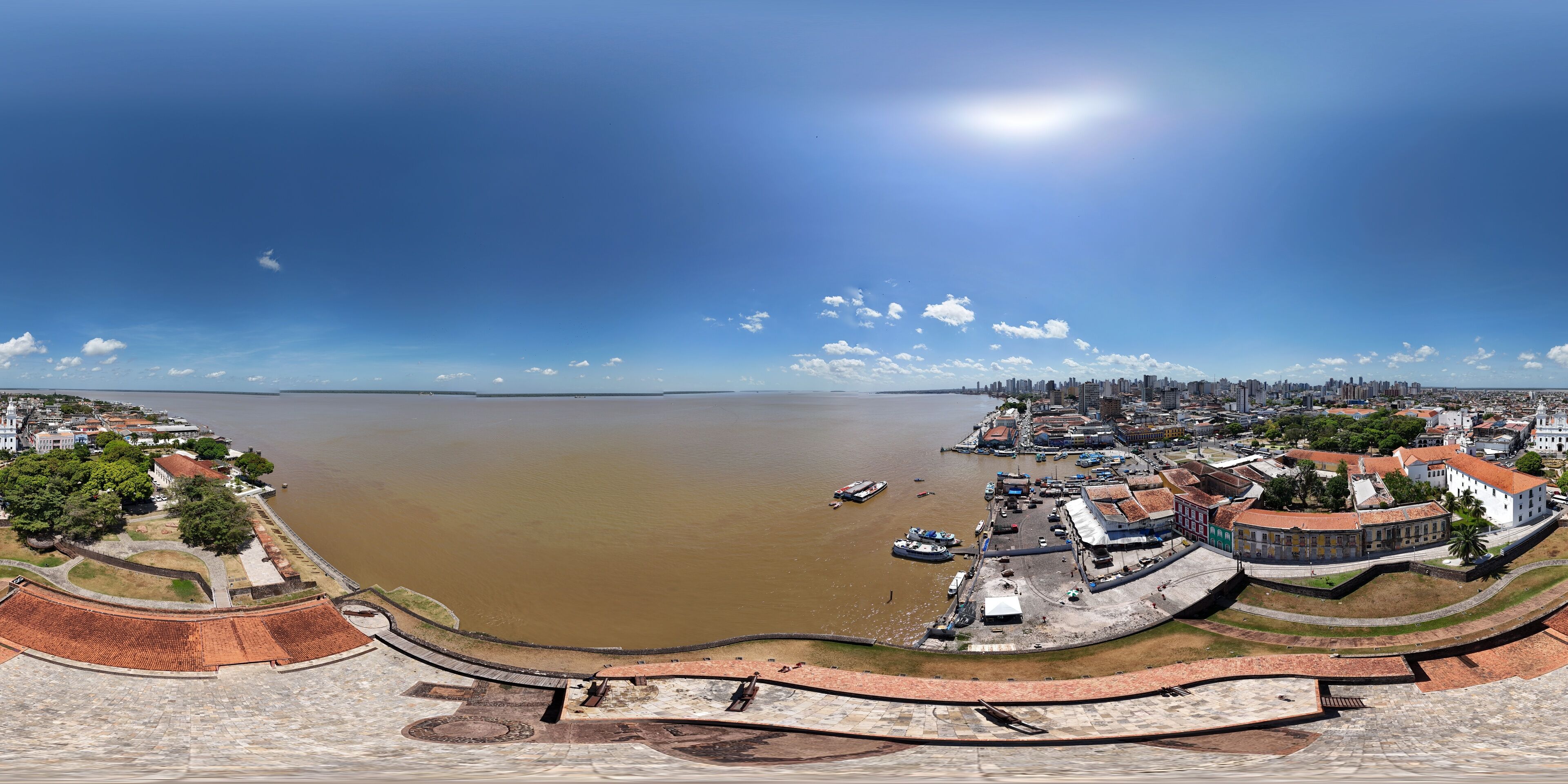 A panoramic view of a coastal city with a large body of water, historic buildings, and a fortified structure.