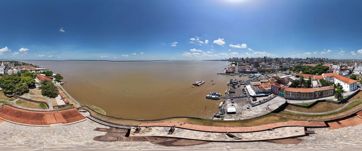 A panoramic view of a coastal city with a large body of water, historic buildings, and a fortified structure.