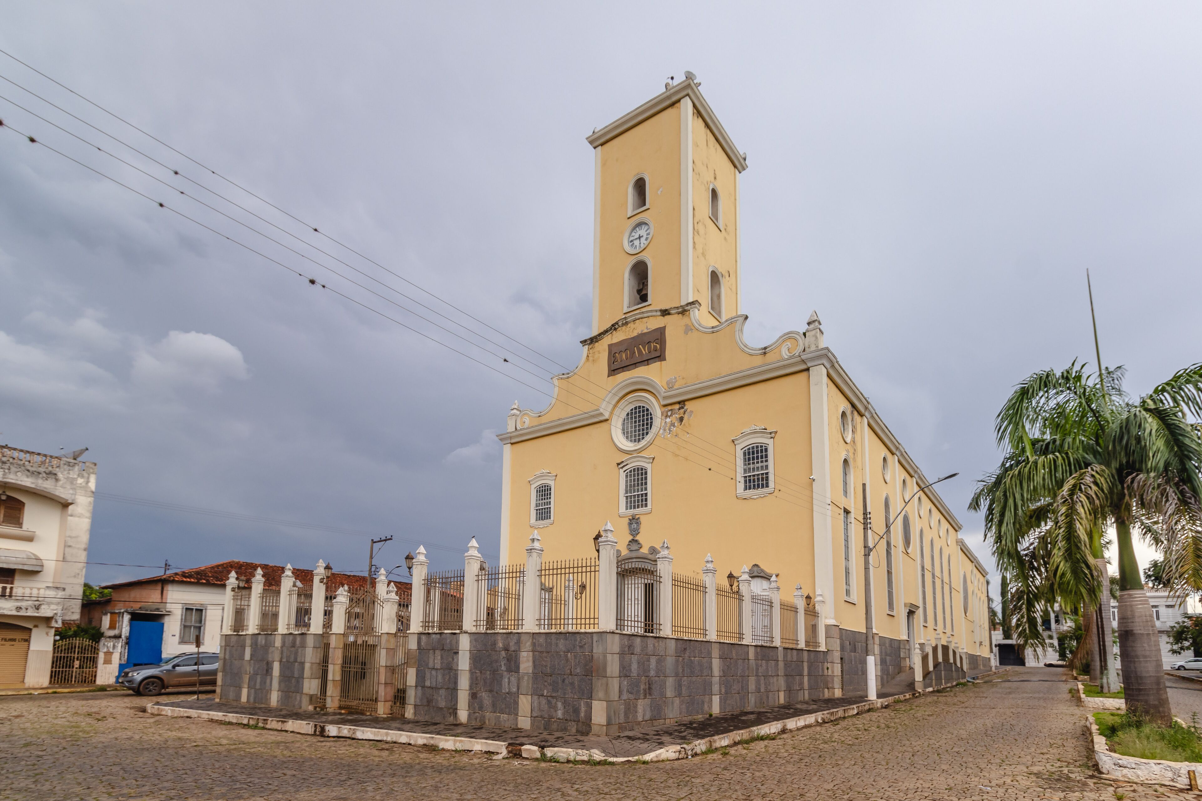 A yellow church with a bell tower and a stone wall in front.