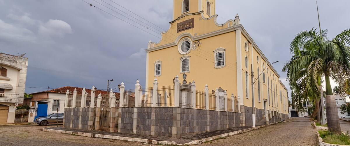 A yellow church with a bell tower and a stone wall in front.