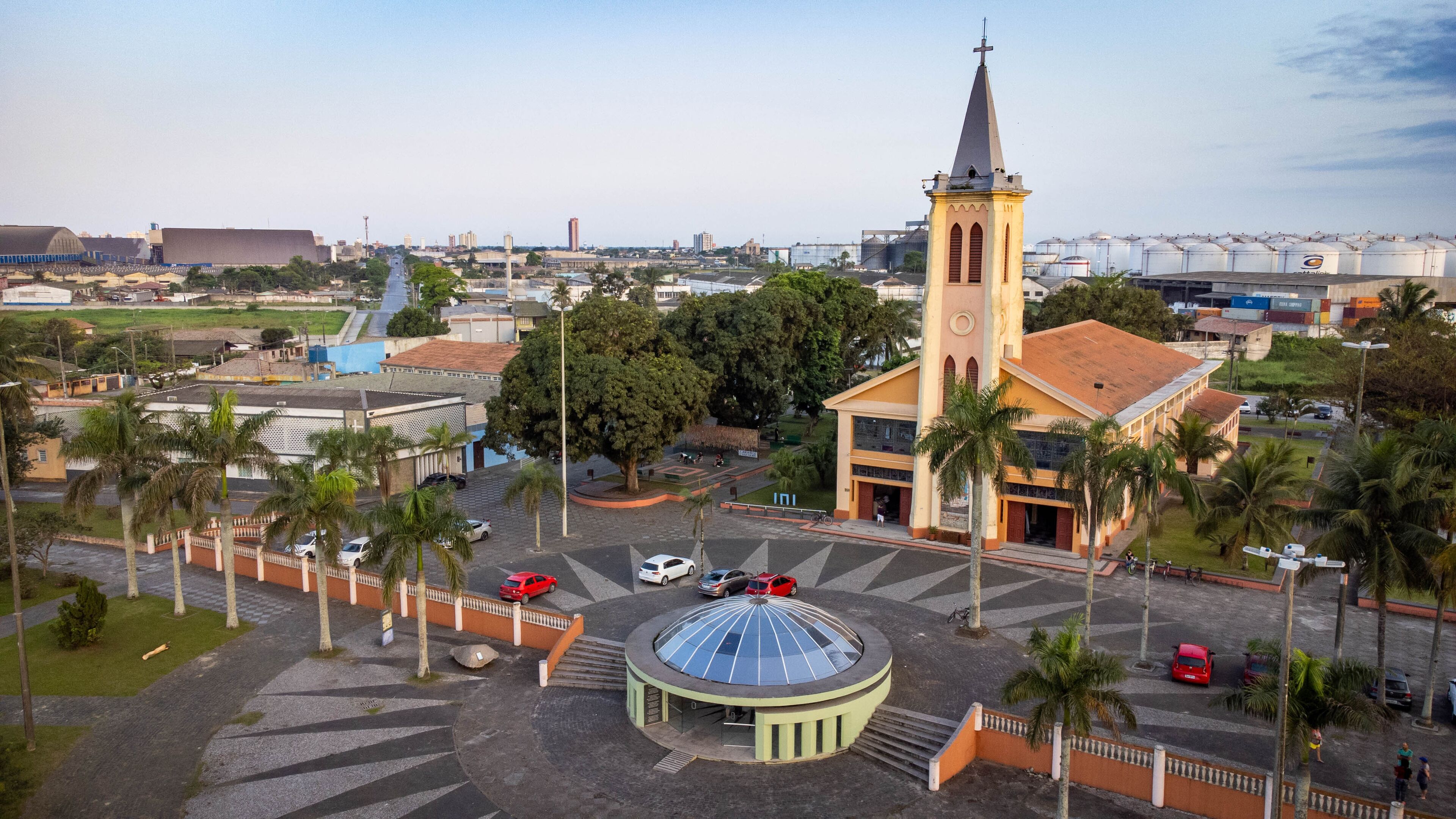 A church with a tall steeple, a round building with a dome, and palm trees.
