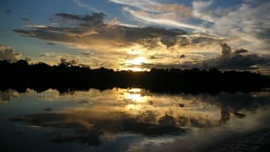 A sunset over a calm lake with clouds reflecting on the water.