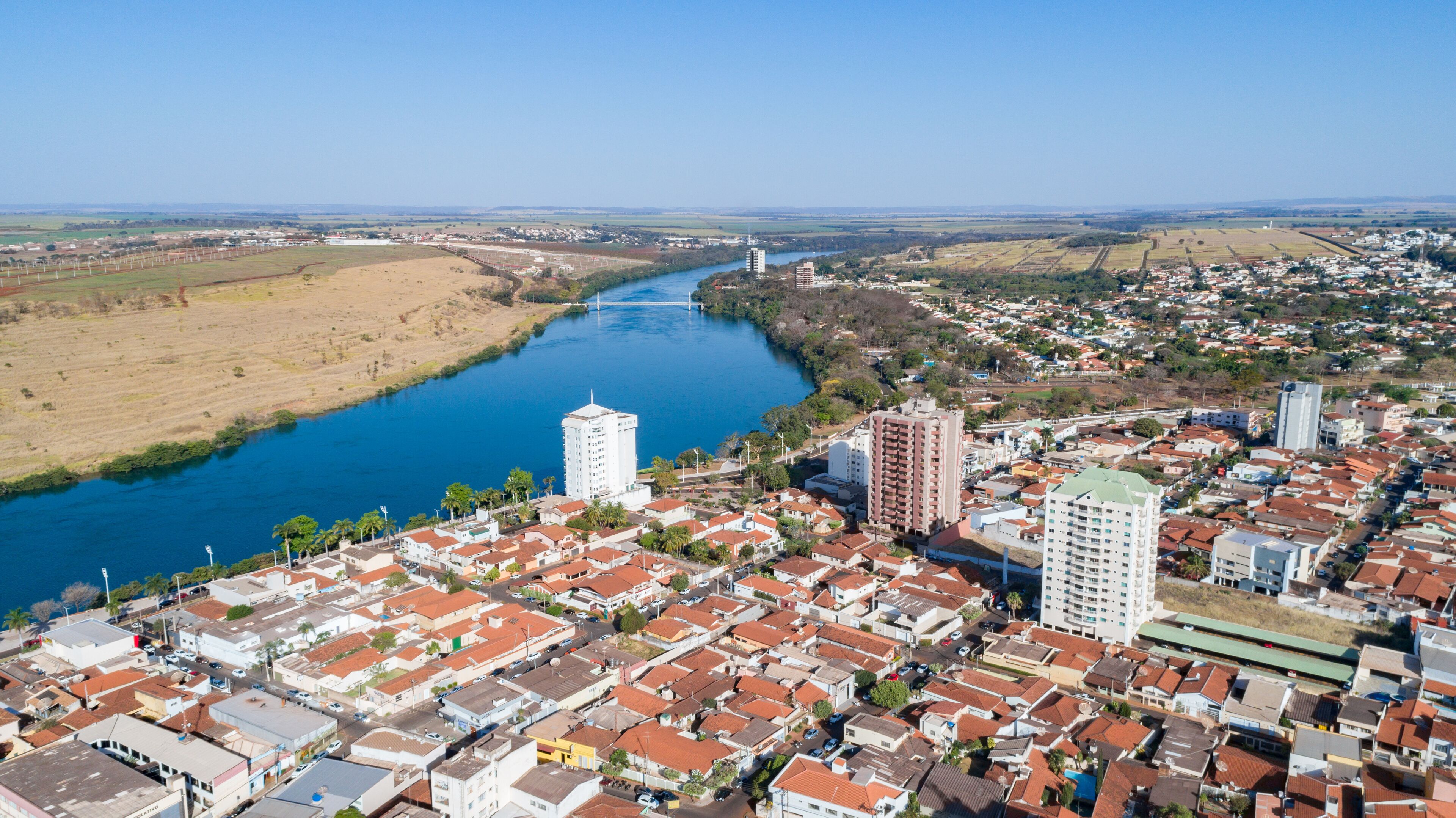 A river flowing through a town with red-roofed buildings and a bridge in the distance.