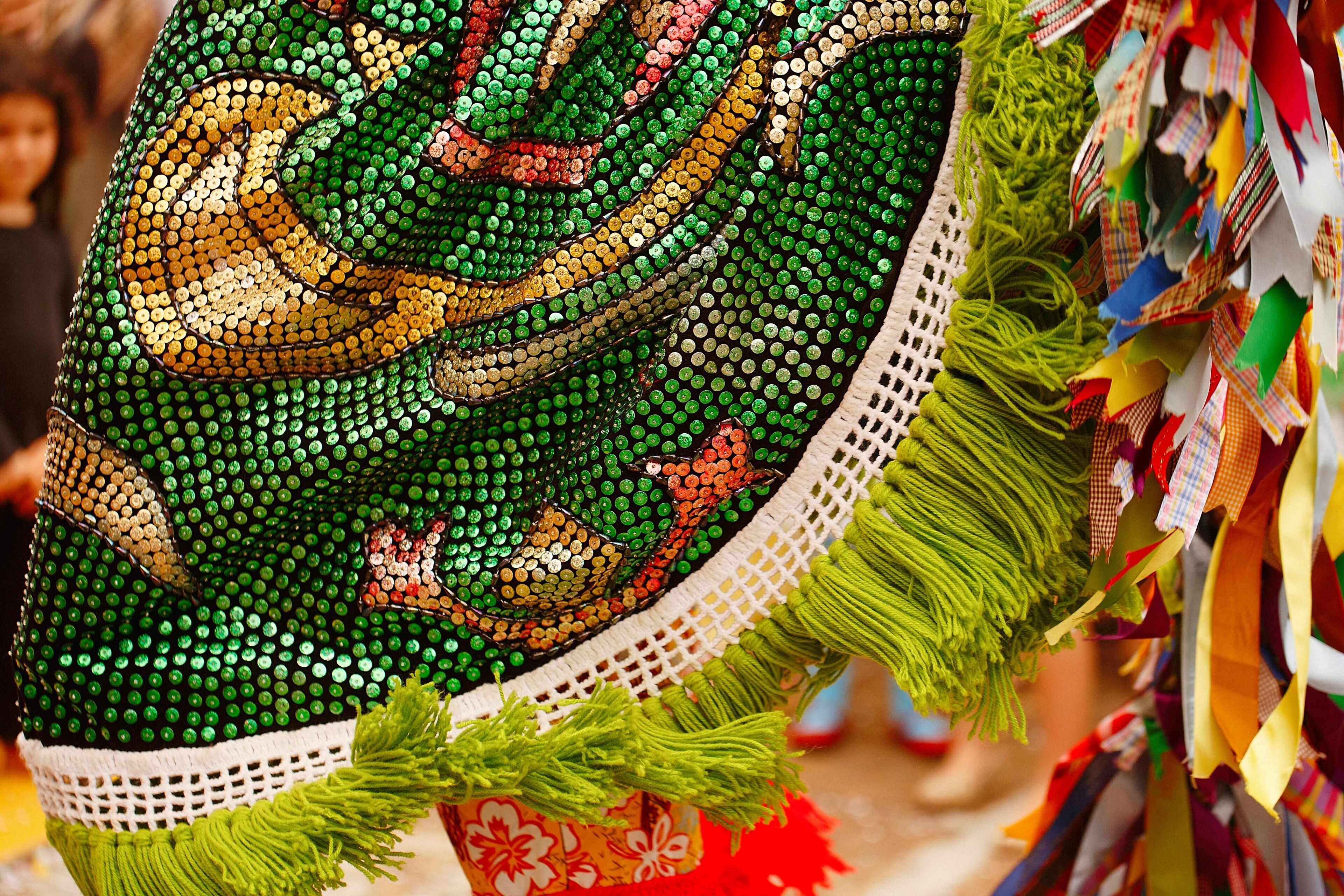 A decorative fabric with a green dragon design, fringes, and colorful tassels.