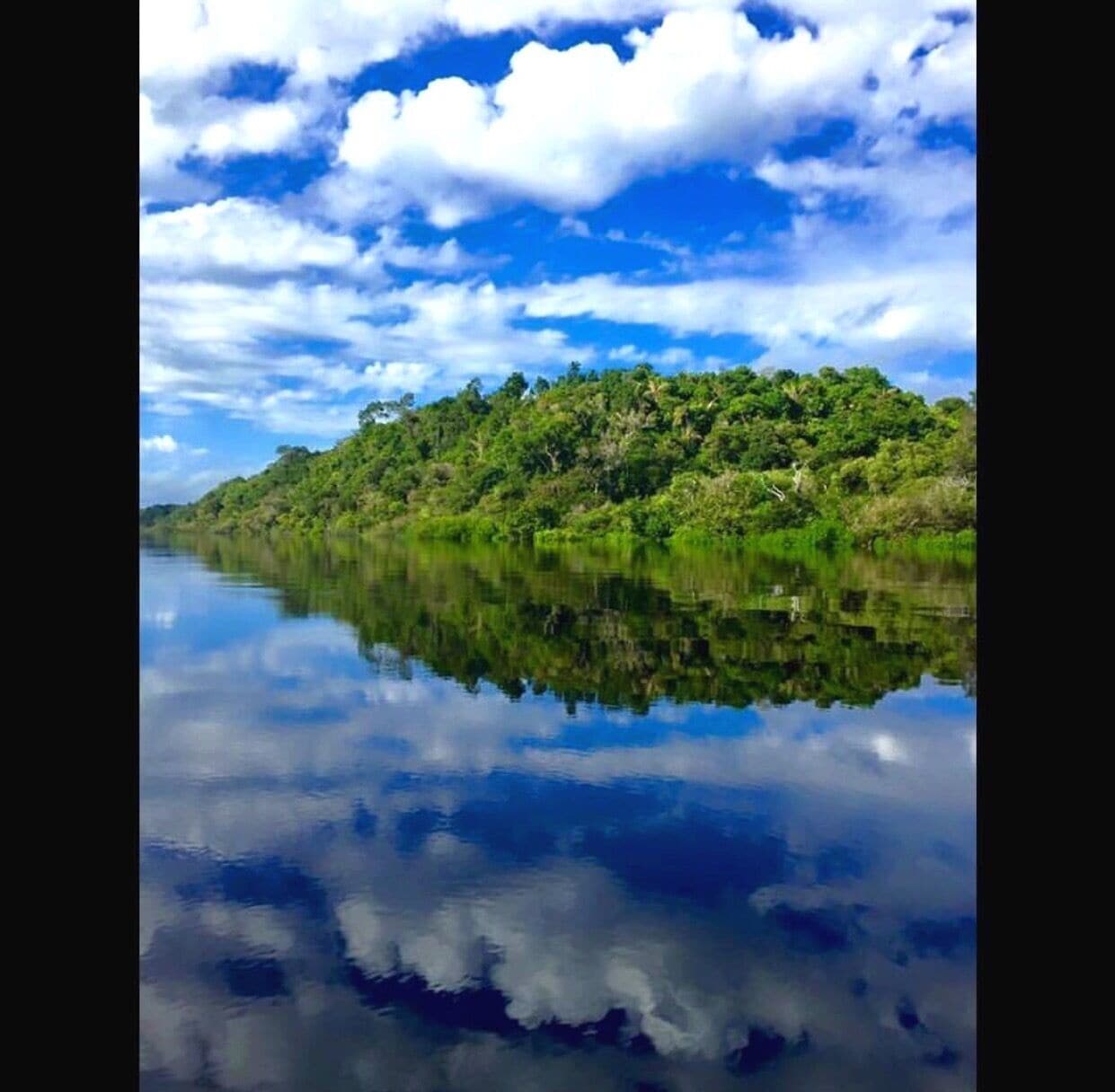 Un riu tranquil que reflecteix el cel i un turó verd i frondós.