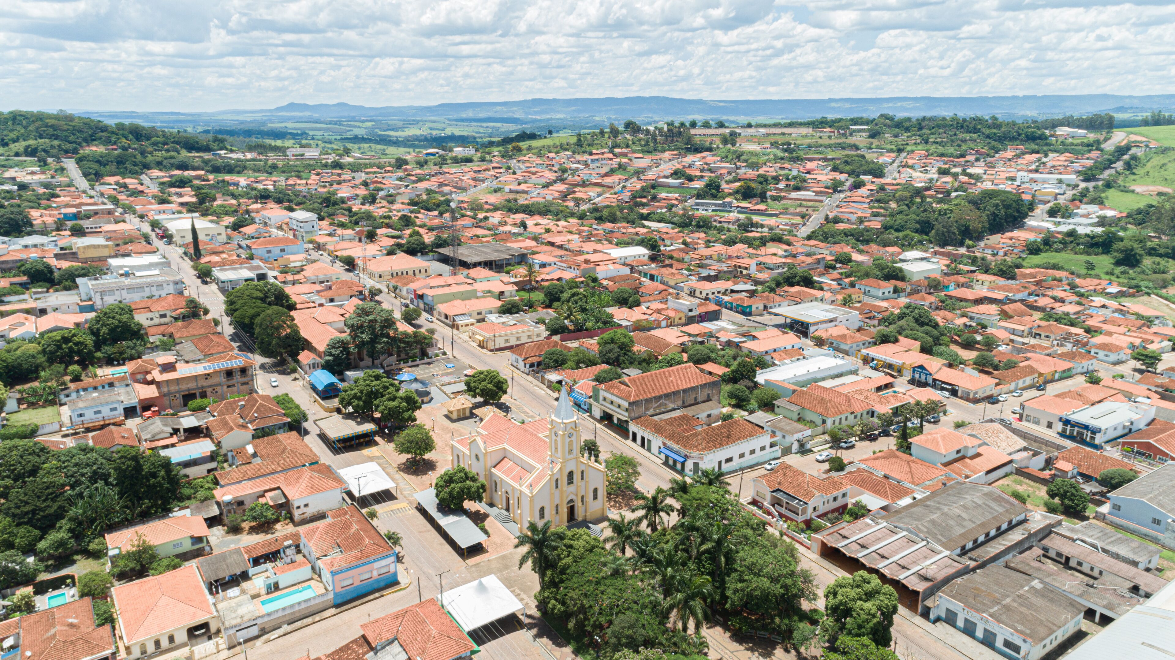 A densely populated urban area with red-roofed buildings, a prominent church, and surrounding greenery.
