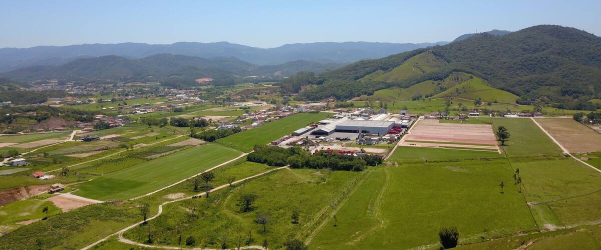 A rural landscape with a large industrial complex, green fields, and rolling hills in the background.