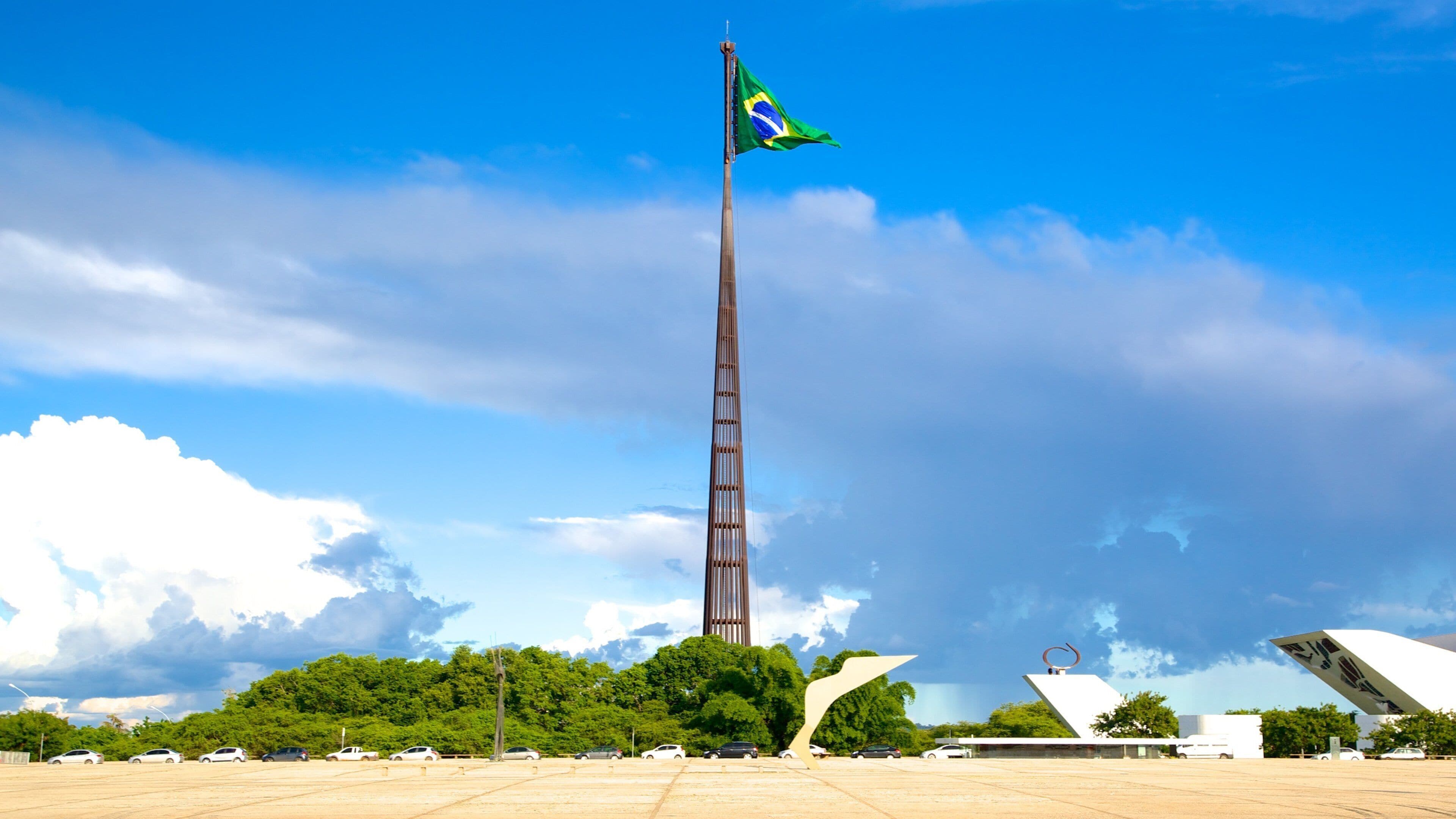 Uma torre alta com uma bandeira, cercada por árvores e arquitetura moderna.