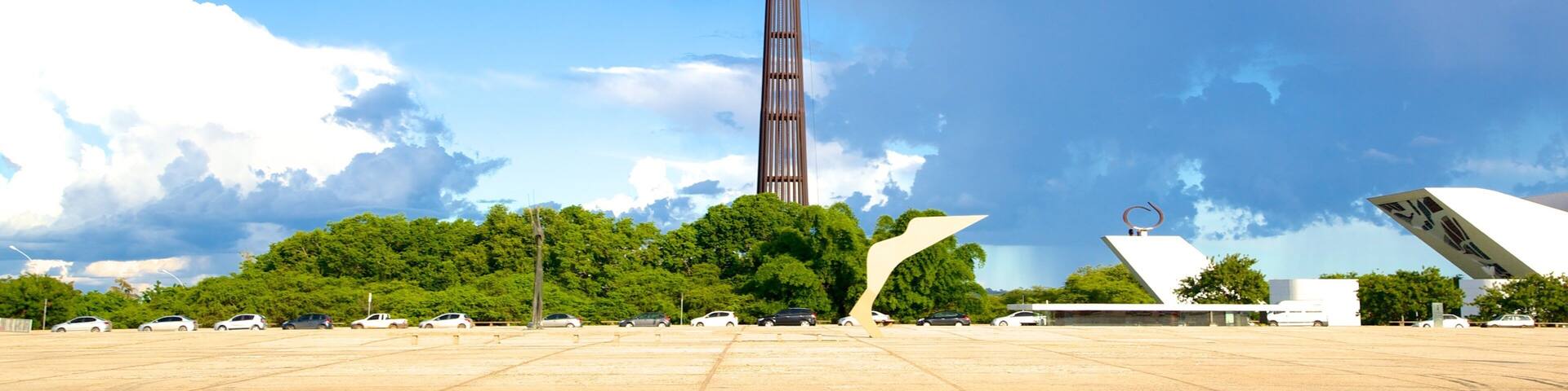 A tall tower with a flag, surrounded by trees and modern architecture.