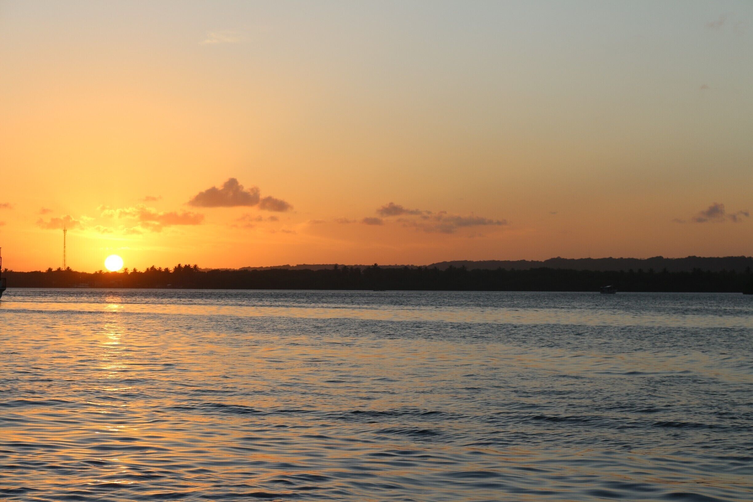 A sunset over a calm body of water with a silhouette of a city skyline in the background.