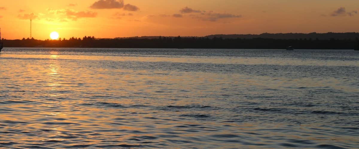 A sunset over a calm body of water with a silhouette of a city skyline in the background.