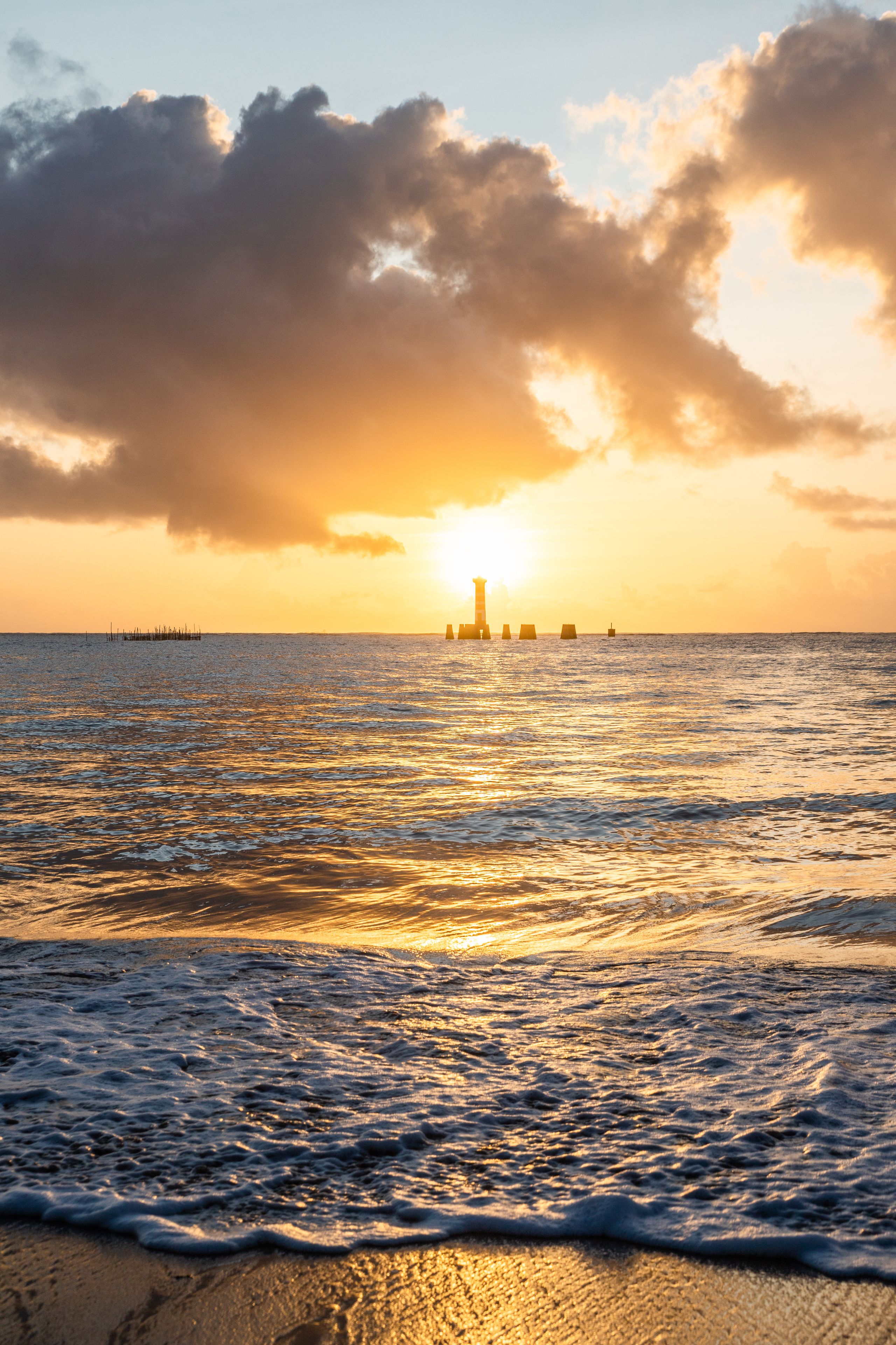 Un coucher de soleil sur une mer calme, avec un phare à l'horizon.