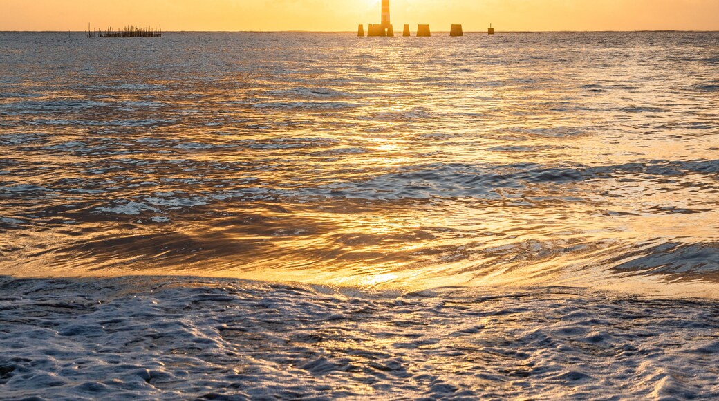 Un coucher de soleil sur une mer calme, avec un phare à l'horizon.