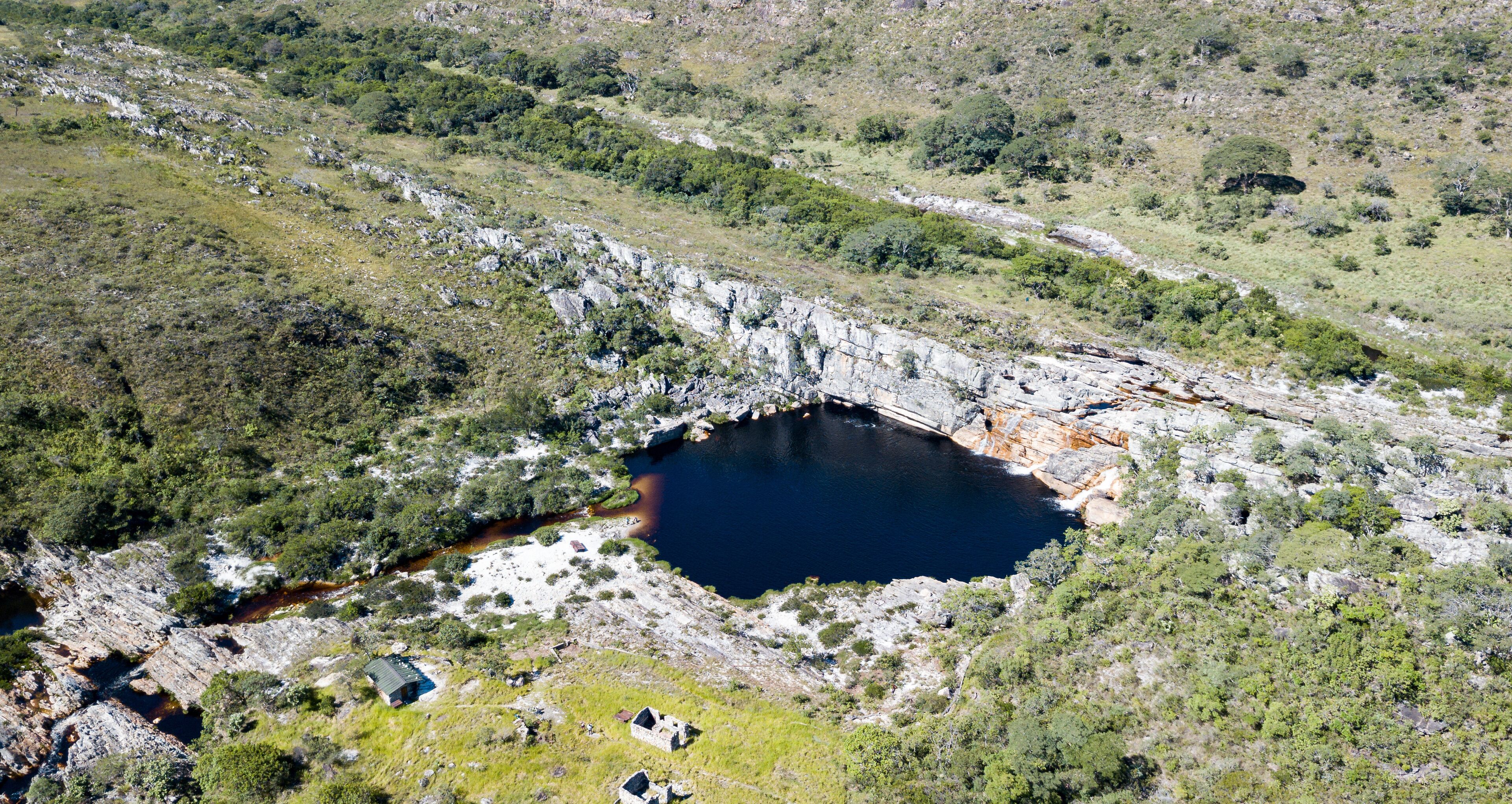 A rocky landscape with a small lake surrounded by greenery and a few buildings.