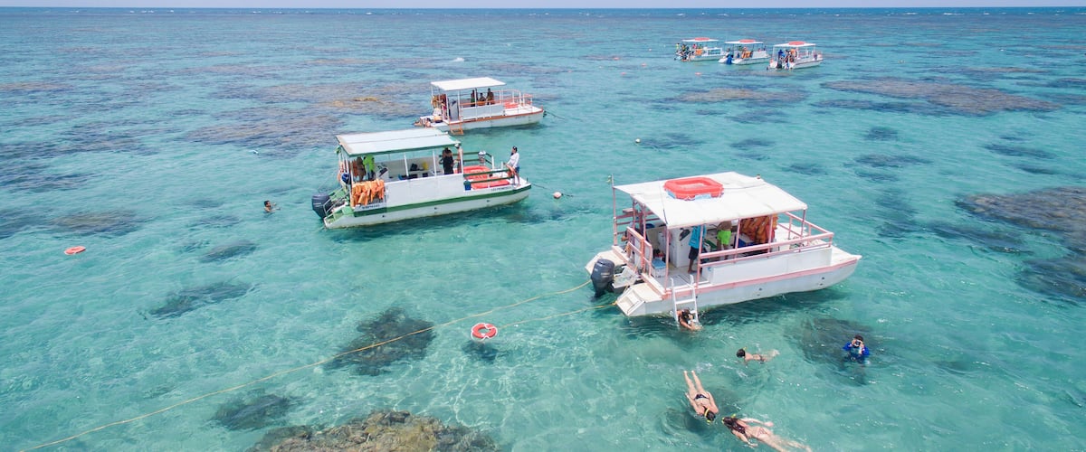 Several boats on clear turquoise water with people swimming and snorkeling.