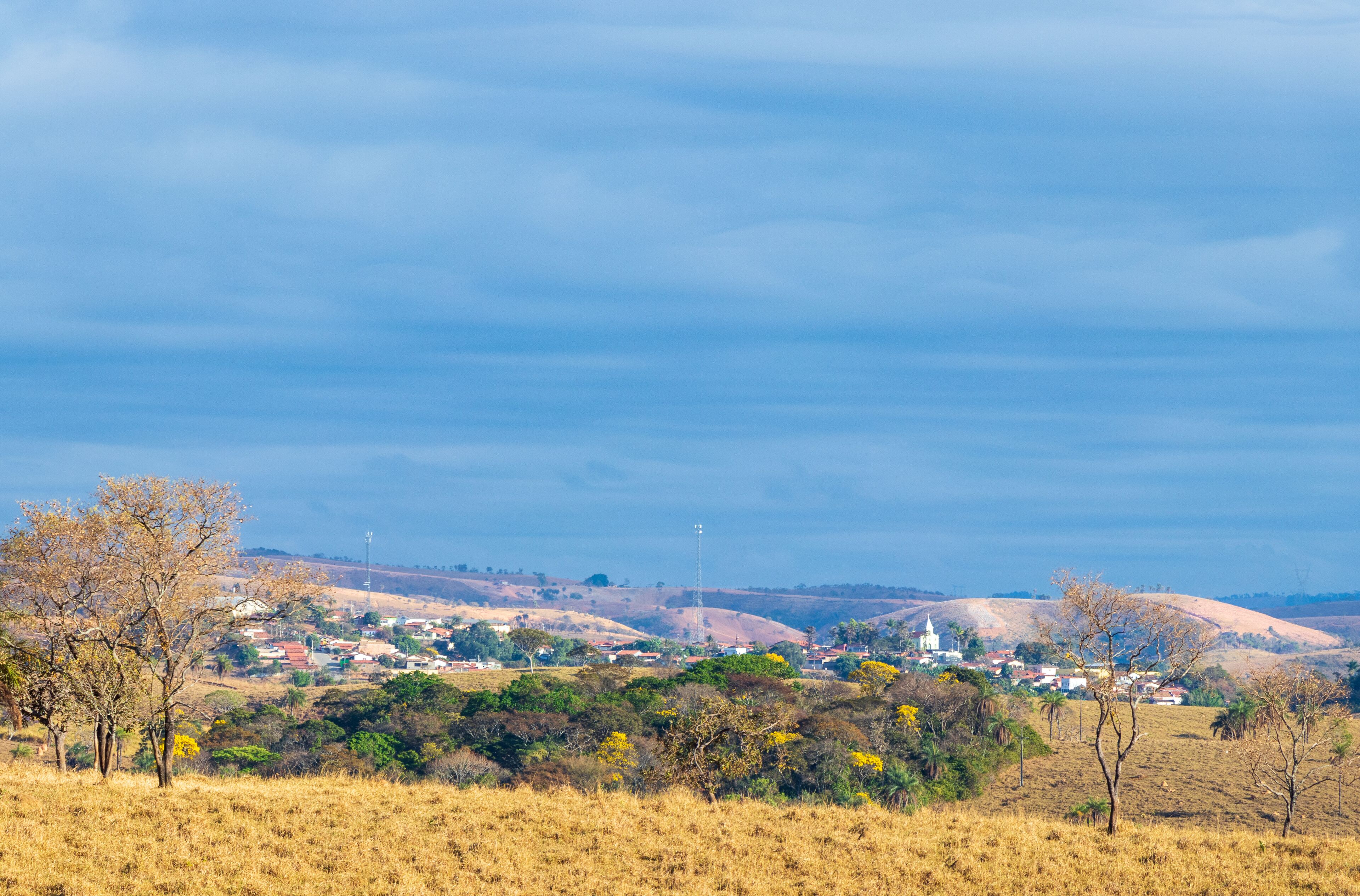 A rural landscape with a small town, rolling hills, and sparse vegetation.