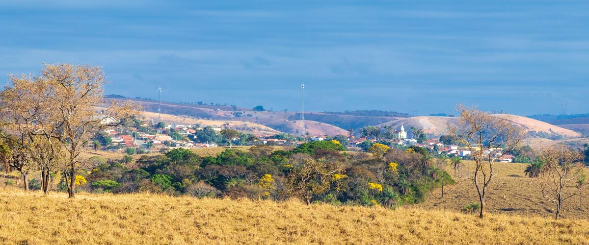 A rural landscape with a small town, rolling hills, and sparse vegetation.