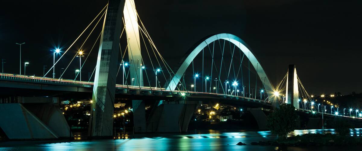 A nighttime view of a large, illuminated bridge with two main arches and multiple cables.