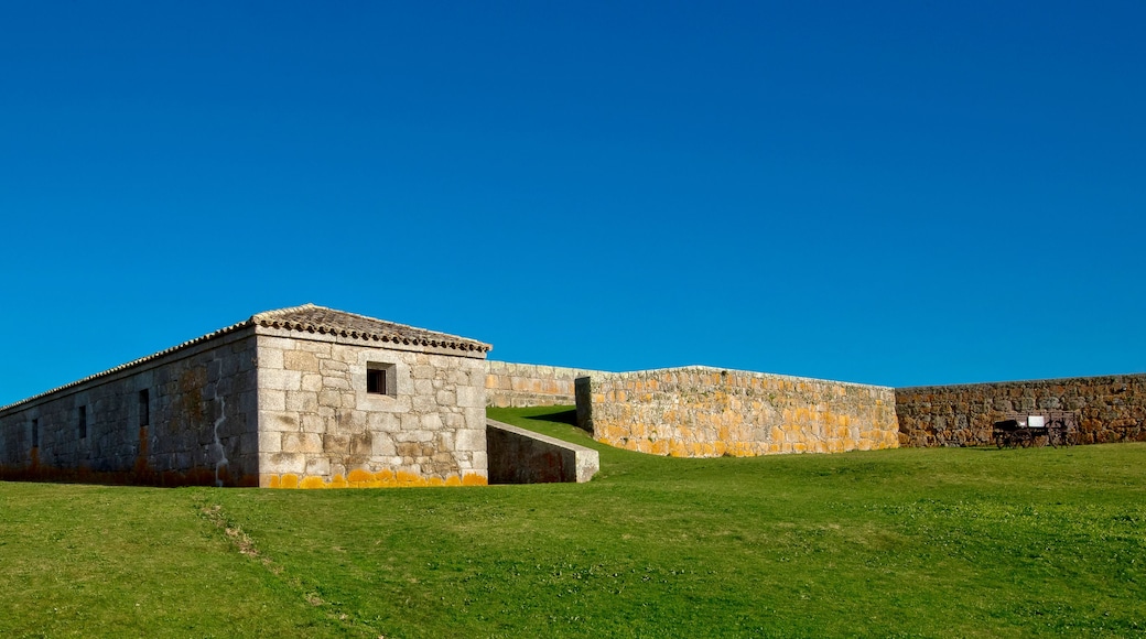 Un edificio de piedra con techo de tejas, un campo cubierto de césped y un cielo azul despejado.