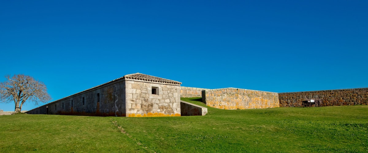 A stone building with a tiled roof, a grassy field, and a clear blue sky.