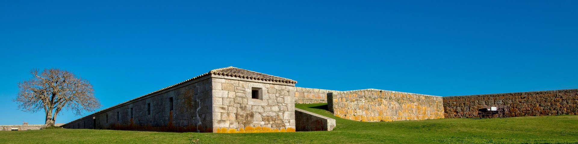 Um edifício de pedra com telhado ladrilhado, um campo gramado e um céu azul límpido.