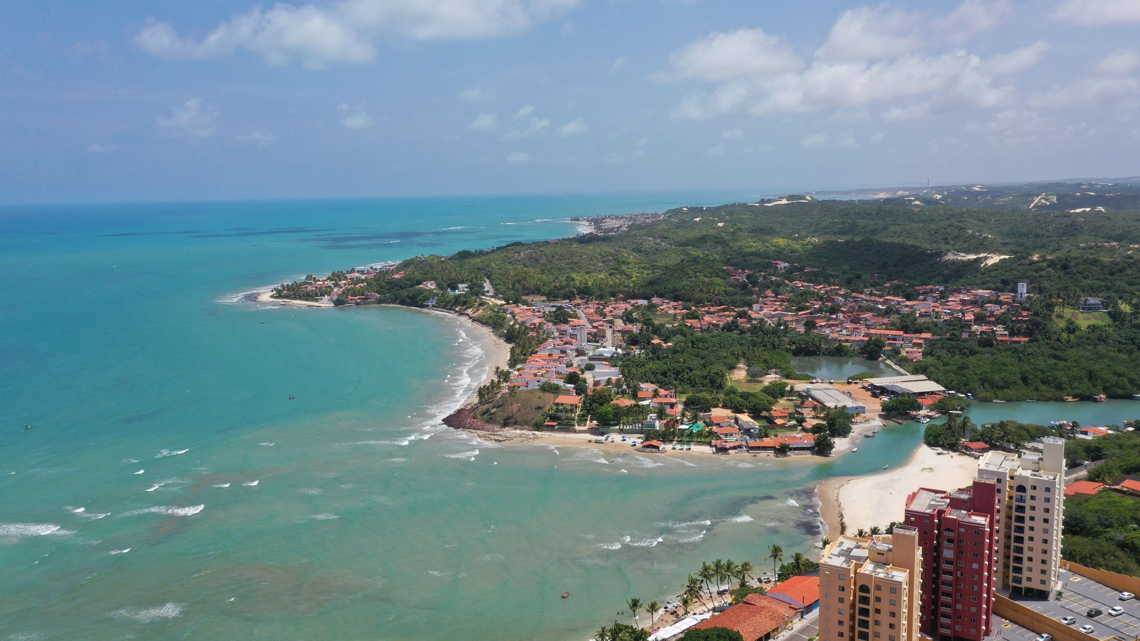A coastal town with a beach, clear turquoise waters, and dense greenery.