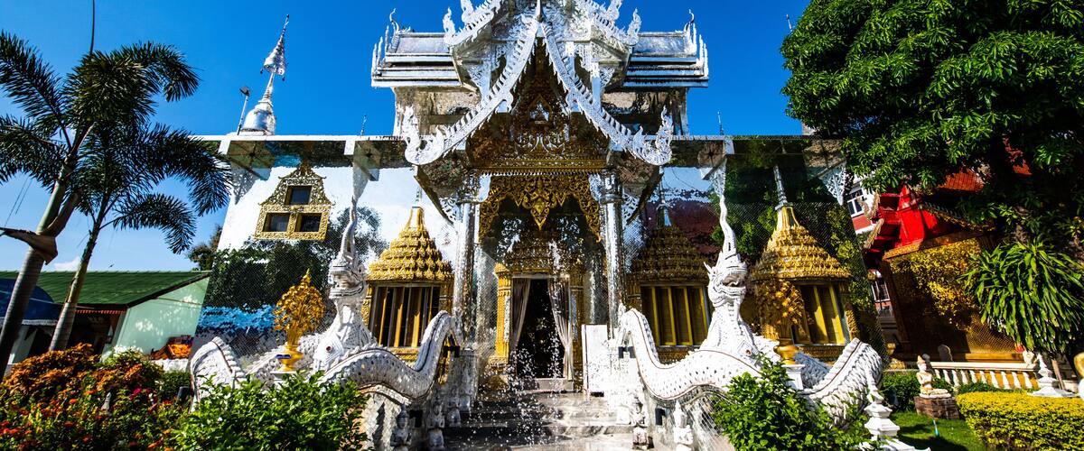A traditional Thai temple with ornate architecture, a central entrance, and a surrounding garden.