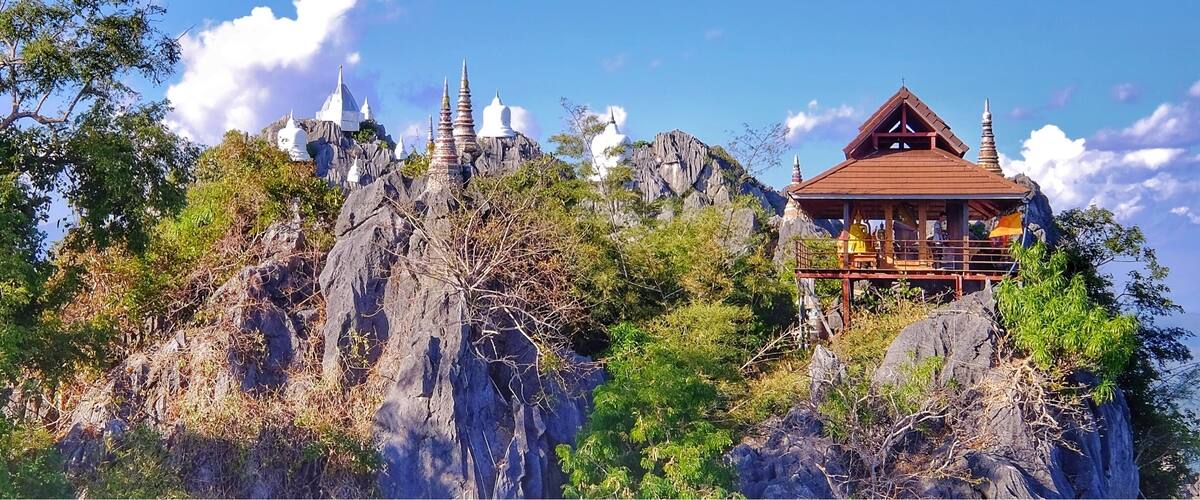 A temple on a rocky mountain with multiple spires and a wooden structure with a red roof.