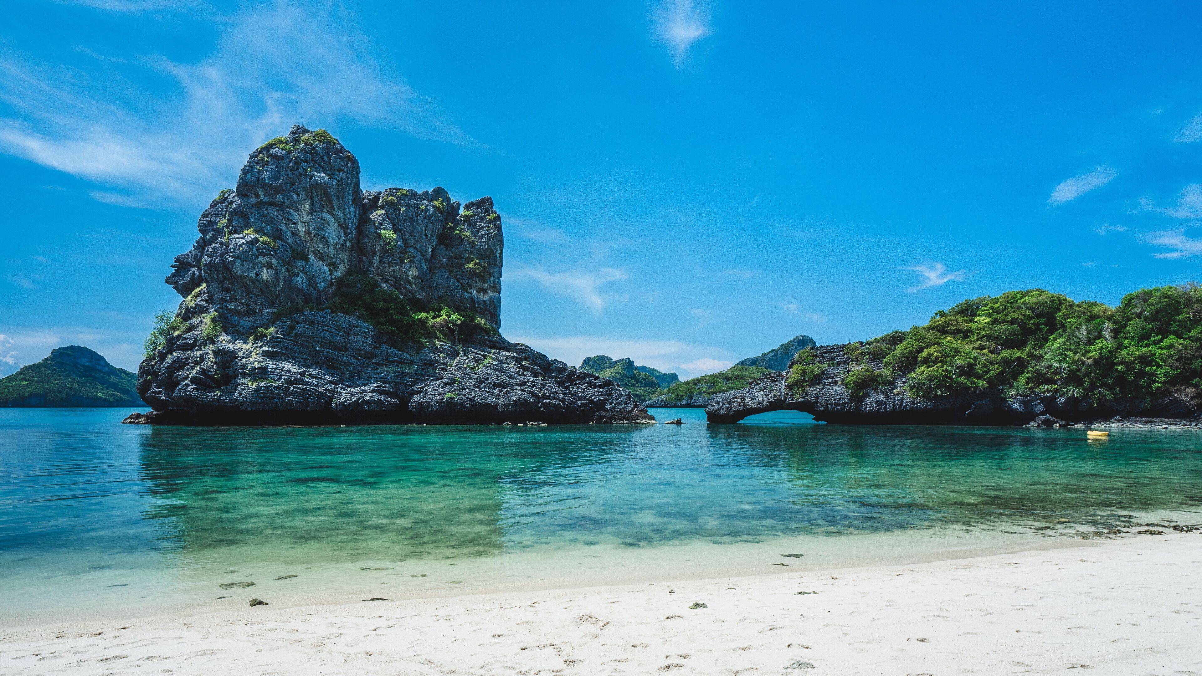 A clear blue sea, a sandy beach, and a rocky formation with a bridge.