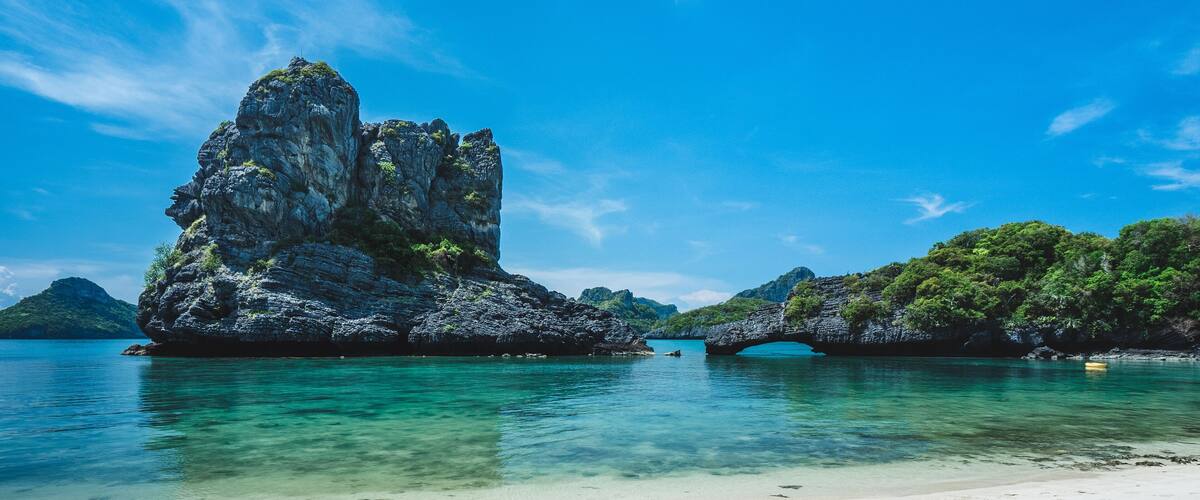 A clear blue sea, a sandy beach, and a rocky formation with a bridge.
