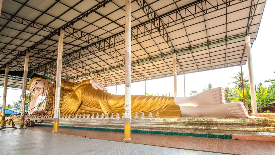 A large reclining Buddha statue under a metal roof.