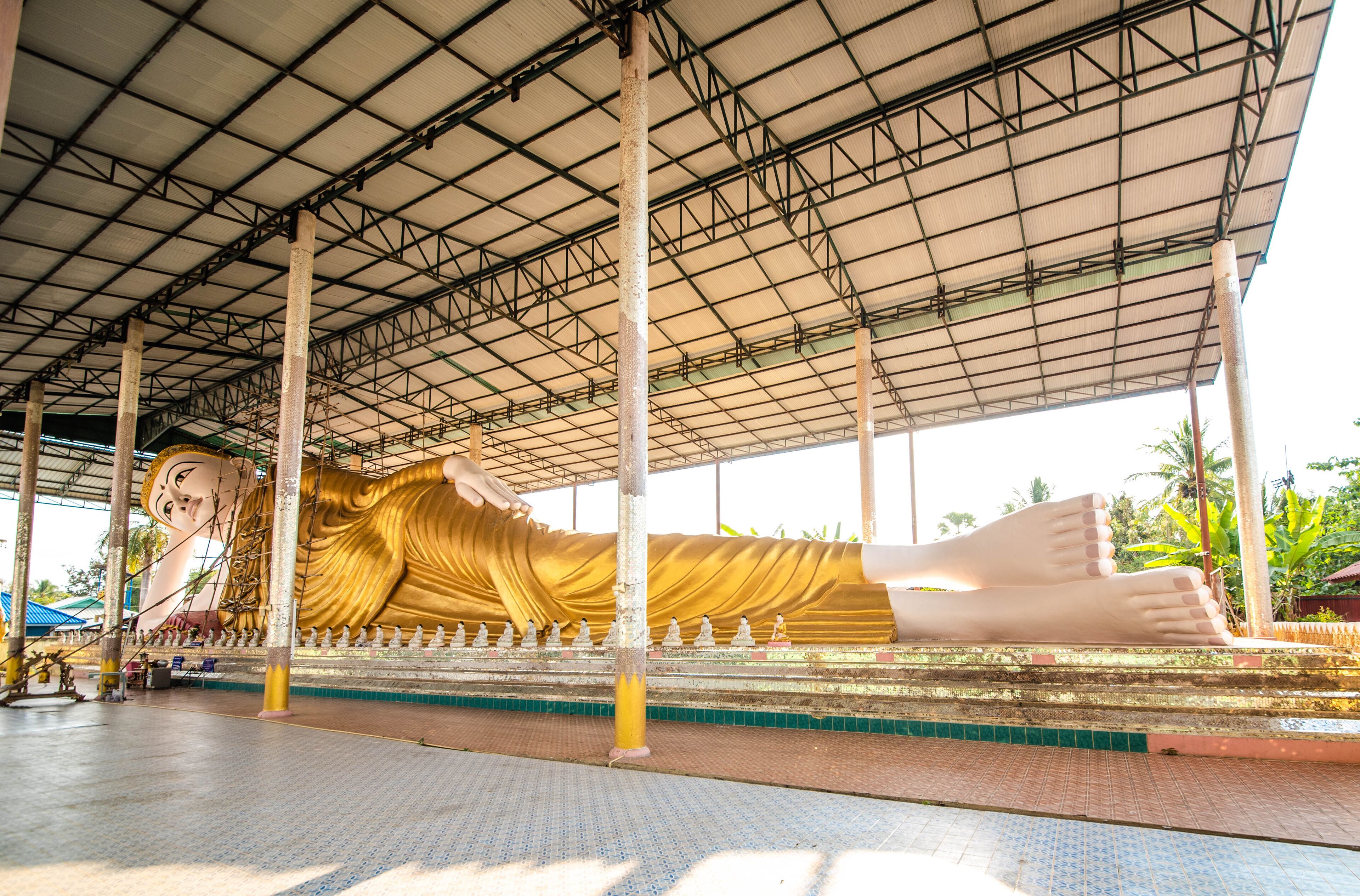 A large reclining Buddha statue under a metal roof.