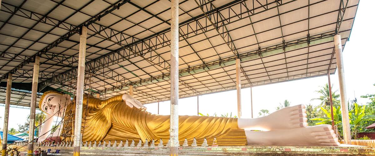 A large reclining Buddha statue under a metal roof.