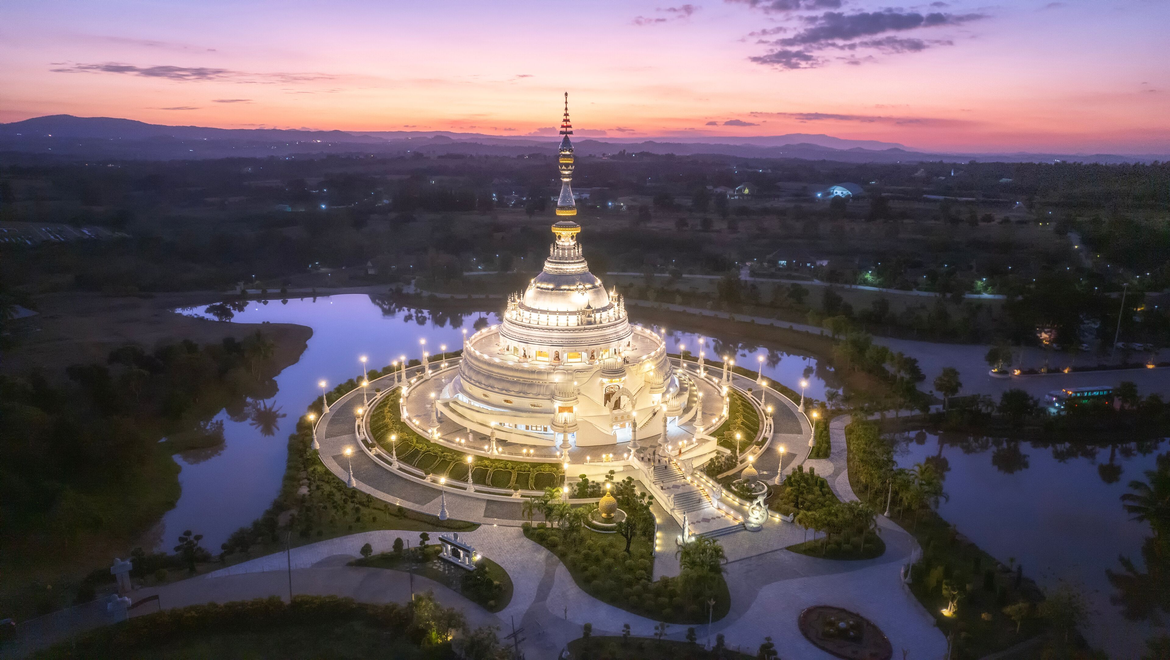 A large, illuminated pagoda surrounded by a lake and gardens at dusk.
