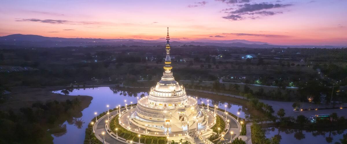 A large, illuminated pagoda surrounded by a lake and gardens at dusk.