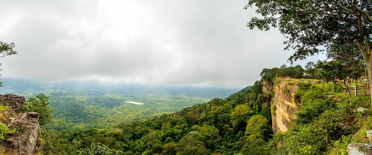 A lush green valley with a stone structure on a cliff edge.