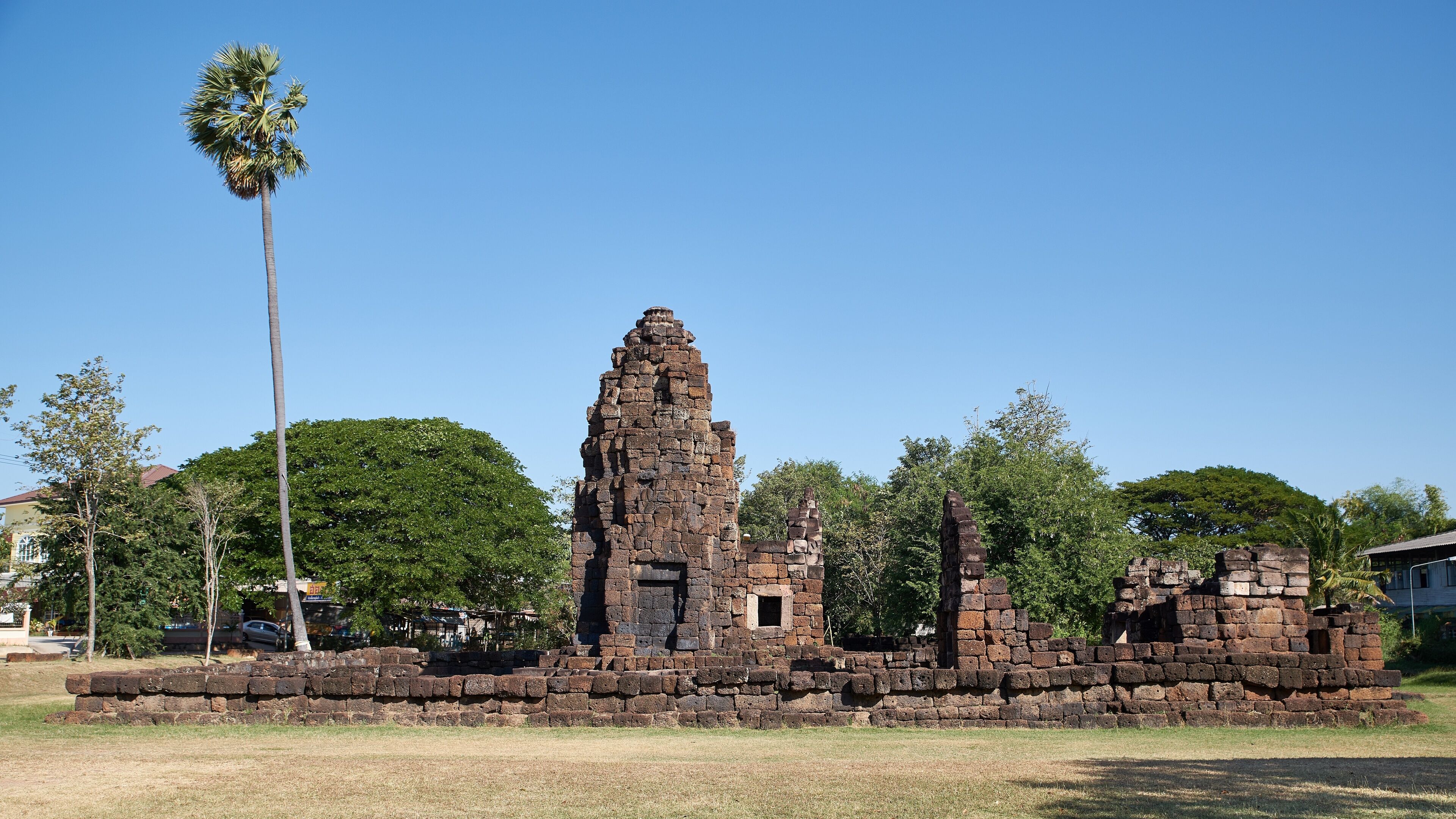 An ancient stone structure with a central tower and smaller buildings, surrounded by trees and grass.