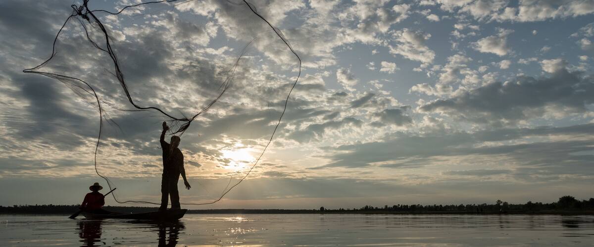 A sunset over a calm body of water with people fishing.