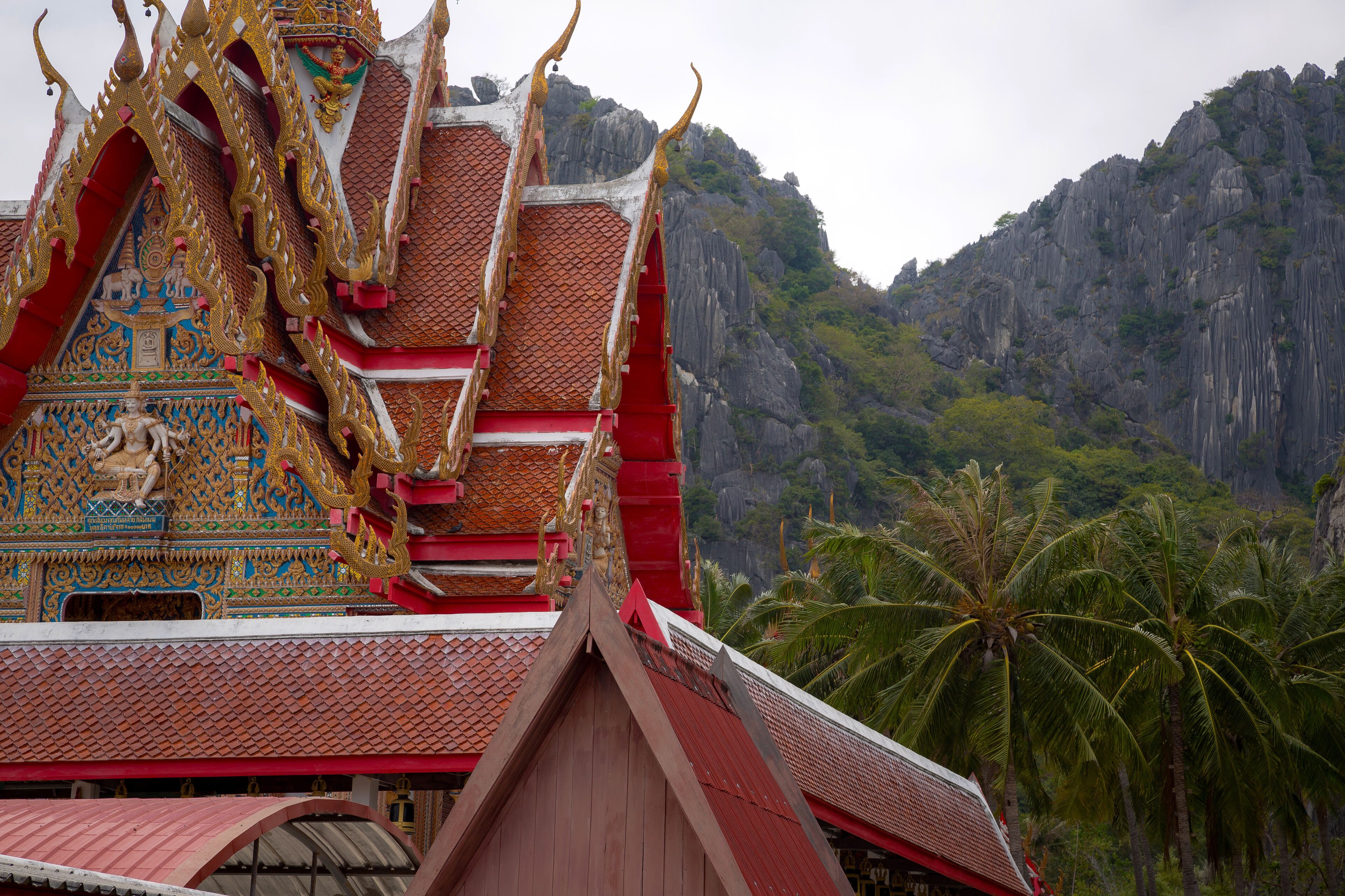 A traditional Thai temple with ornate architecture and a mountainous backdrop.