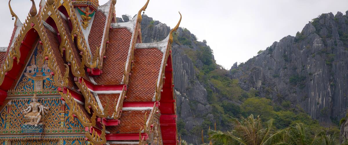A traditional Thai temple with ornate architecture and a mountainous backdrop.