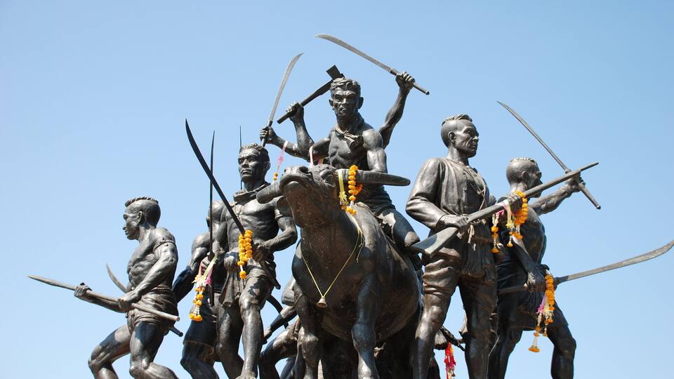 A bronze statue of warriors on horseback with swords, set against a clear blue sky.