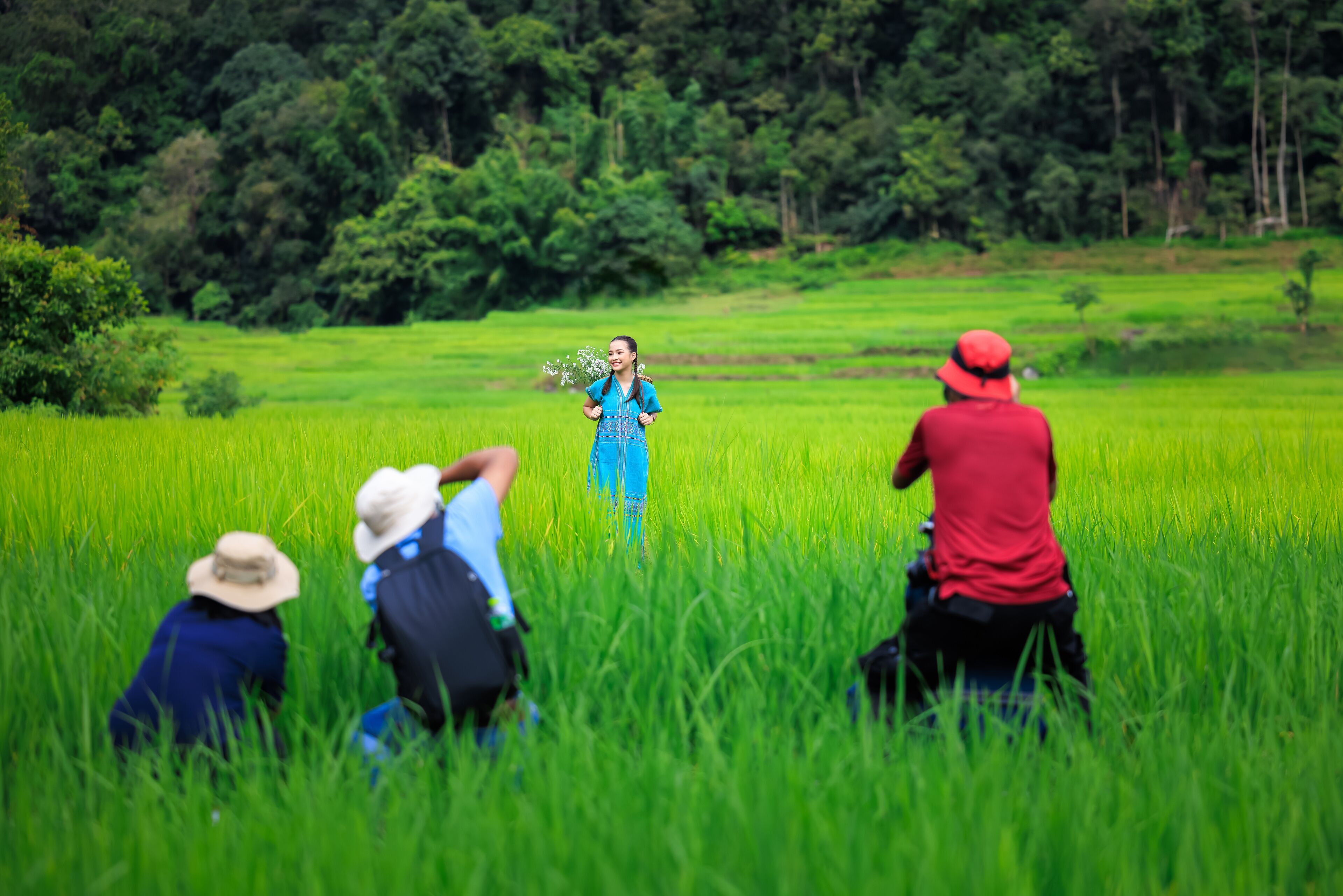A person in a blue dress standing in a lush green field with three people in the foreground.