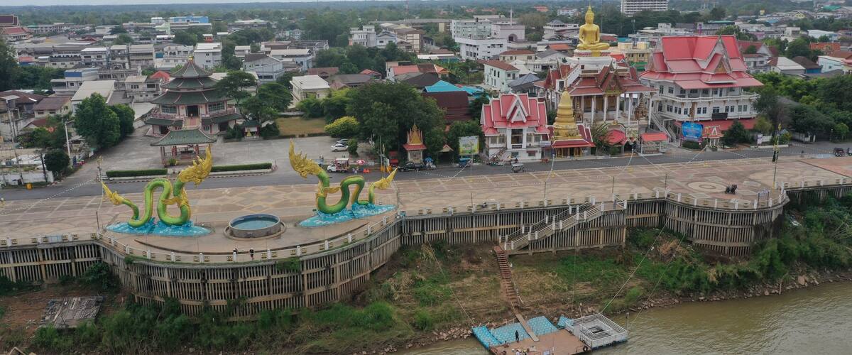 A river with a boat, a large golden statue, and a temple with a red roof.