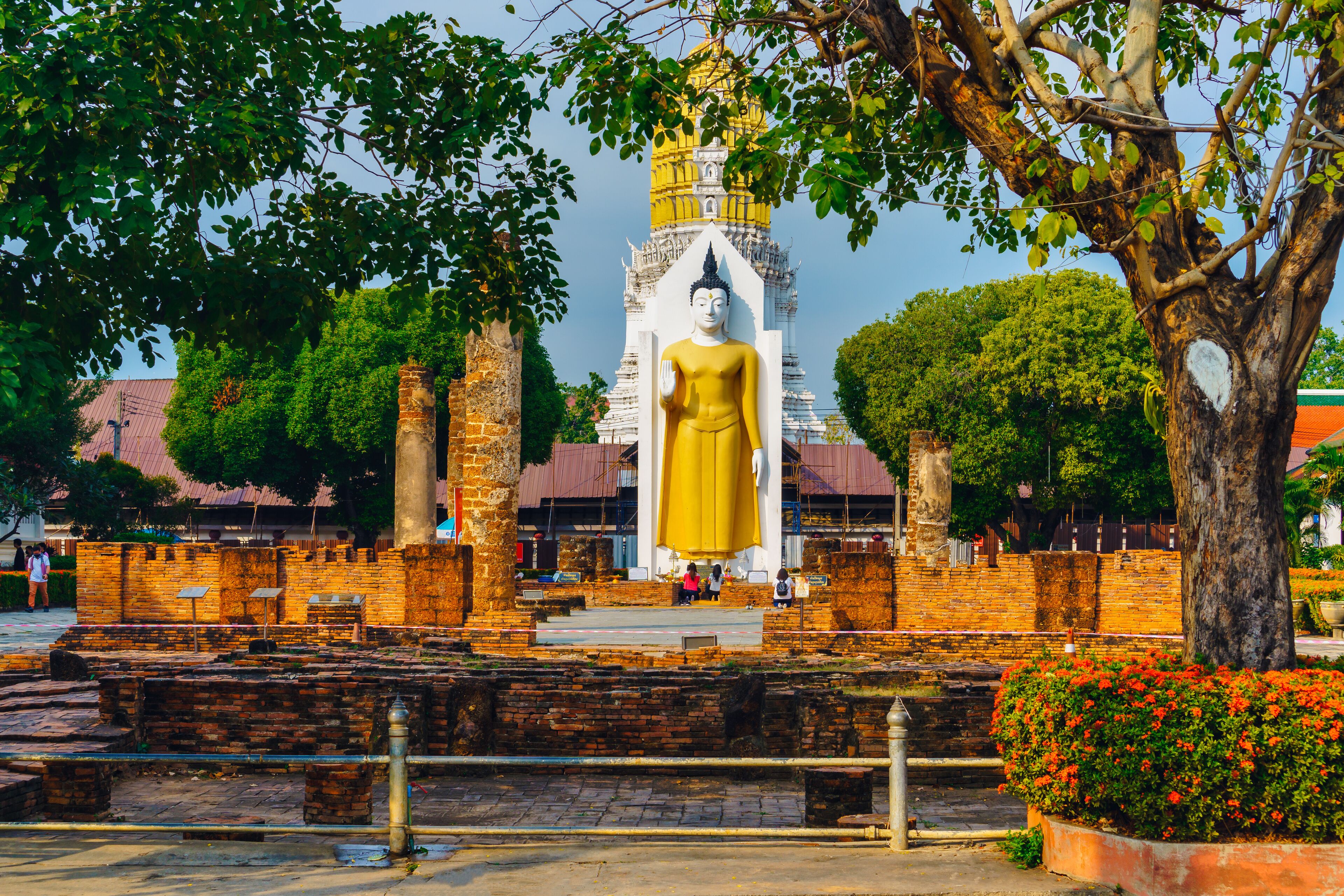 A large golden statue in front of a temple with a yellow spire.